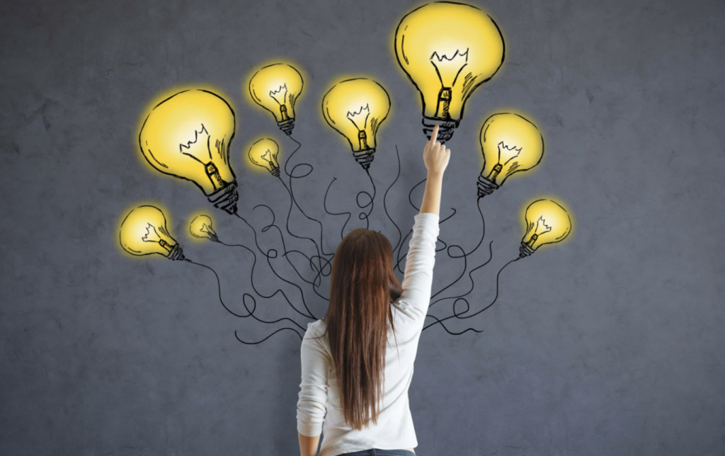 Woman reaching toward glowing yellow light bulbs on a gray wall, symbolizing creativity and inspiration